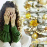 woman holding her face in her hands sitting by a christmas tree demonstrating the christmas effect on moood